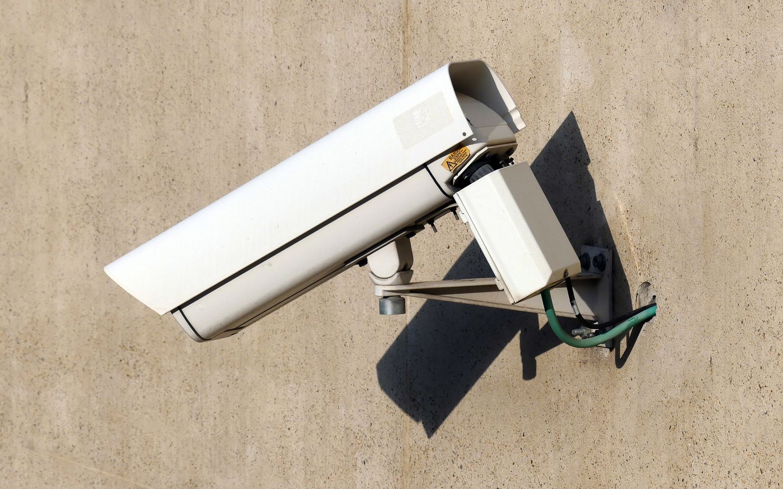 Close-up of a white security camera mounted on a beige wall in sunlight, emphasizing safety.